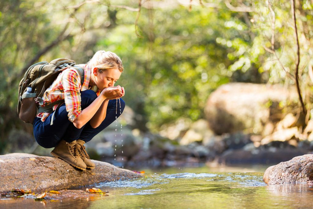 femme qui boit de l'eau d'une rivière randonnée